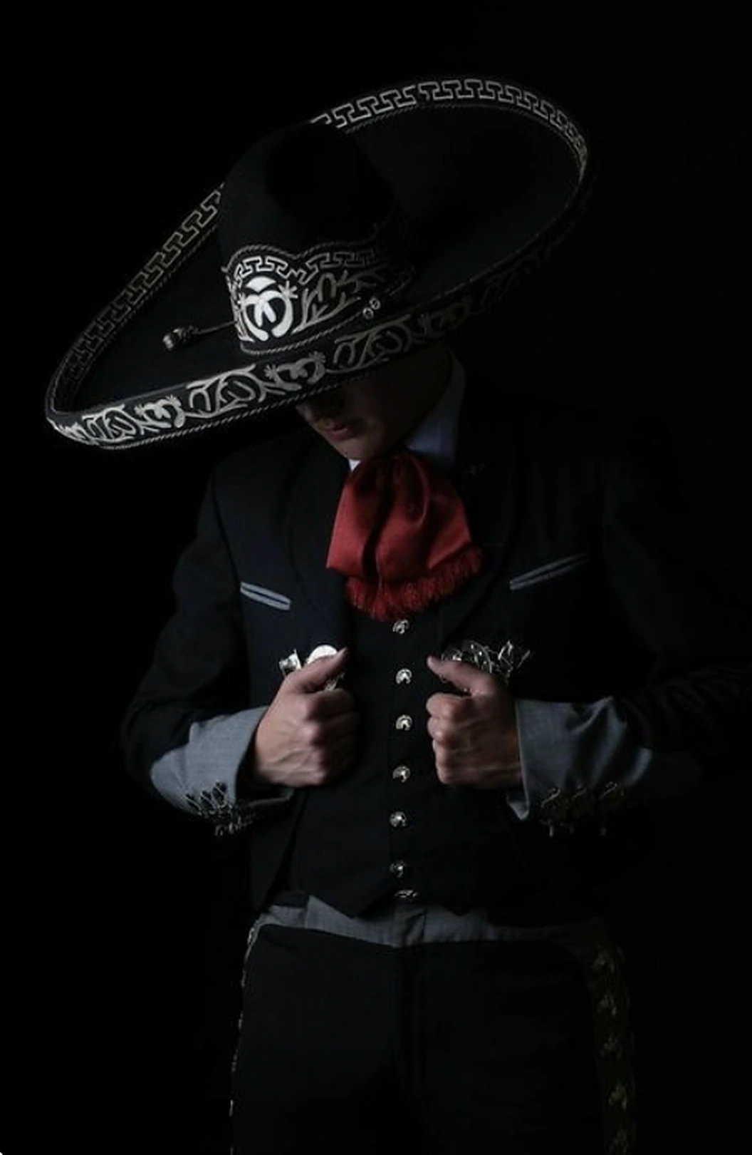 Charro de negro con moño rojo y sombrero bordado, de cabeza baja