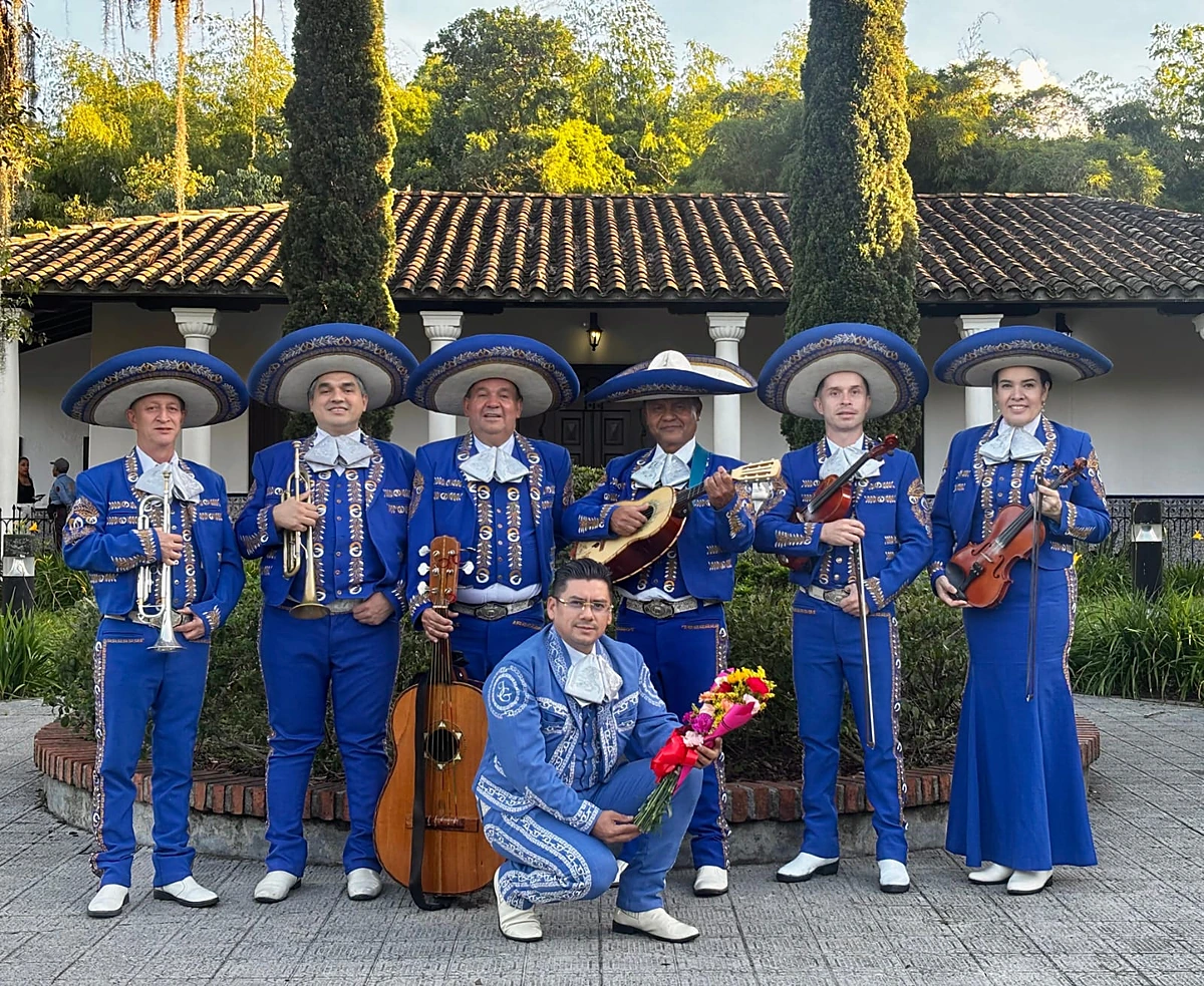 Legado Real de azul rey, con trompetas, violines y guitarrón, frente a una casona entre árboles
