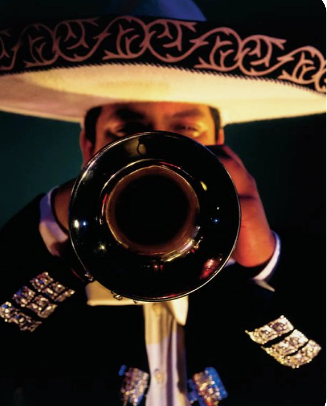 Trompetista de mariachi con sombrero bordado, de frente, con la campana de la trompeta apuntando hacia ti